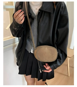 Close-up of minimalist brown suede oval crossbody bag worn by a model in black leather jacket