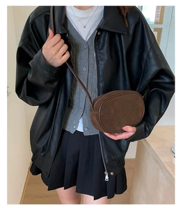 Detail of dark brown oval crossbody bag paired with a retro varsity style outfit