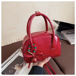 Détail du sac polochon rouge avec texte embossé et breloques décoratives à nœud