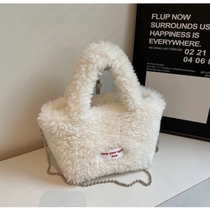 Detail of soft white faux fur handbag with red slogan tag and silver metal chain strap