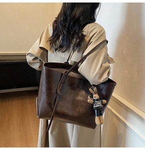 Detail view of deep brown leather tote bag with a cute plaid rabbit plush pendant
