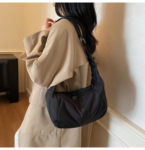 Close-up of a black nylon crescent bag with silver zipper on a model in a beige coat