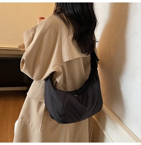 Close-up of black nylon crescent cross-body bag worn with a khaki trench coat