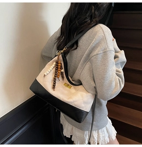 Close-up of beige quilted shoulder bag with black leather trim and wooden bead tassel