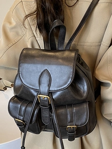 Classic black leather-style backpack with gold buckles worn over a beige trench coat