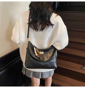 Detail of black quilted shoulder bag featuring vintage beaded charms and gold-tone twist lock
