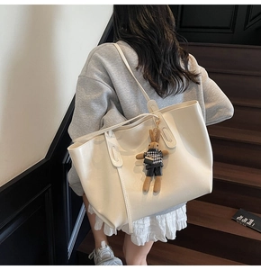 Detail of cream white faux leather tote bag with a small rabbit charm on a wooden staircase