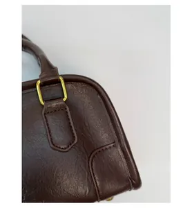 Detail of dark brown leather handbag with gold D-ring hardware and precise stitching