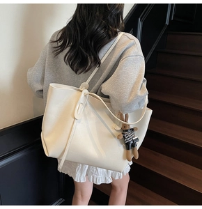 Detail of a creamy white large tote bag with a cute rabbit charm shown on a model