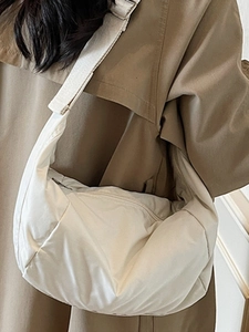 Minimalist beige dumpling bag with adjustable strap worn by model in casual style