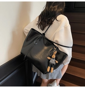 Detail view of large black tote bag with cute plush rabbit charm on a stylish model