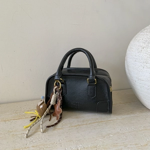 Close-up of black textured leather mini Boston bag with creative charms and gold hardware