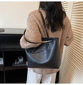 Detail of a large black leather tote bag with fashion lettering and long shoulder straps