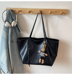 Detail of black faux leather tote bag featuring a cute bunny charm and lychee texture