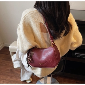 Detail of burgundy leather crescent shoulder bag with gold logo on a model