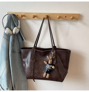 Detail of a brown leather tote bag with a cute rabbit doll charm and vintage texture