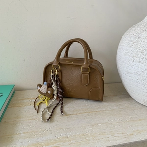 Detail view of brown pebbled leather Boston bag with double handles and bear charm