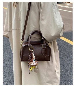 Detail view of brown vintage leather handbag with teddy bear charm on model in street setting