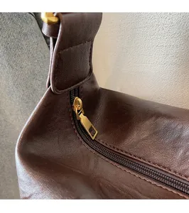 Detail of smooth gold metal zipper puller on dark brown leather crossbody bag