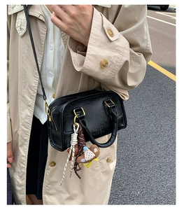 Detail of black lychee grain leather crossbody bag with a cute brown bear charm