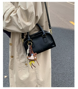 Detail of black lychee leather crossbody bag with cute teddy bear charm and logo