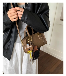 Detail of a brown cylindrical crossbody bag with bear charms and letter embossing