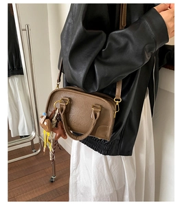 Detailed view of a brown pebbled leather Boston bag with plush doll and star pendants