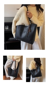 Close-up of black woven tote bag featuring an embossed logo and a brown leather charm
