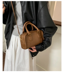 Detail of brown vintage crossbody bag with gold hardware and embossed logo on model