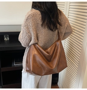 Detail view of large brown PU leather tote bag worn by a model in a warm setting
