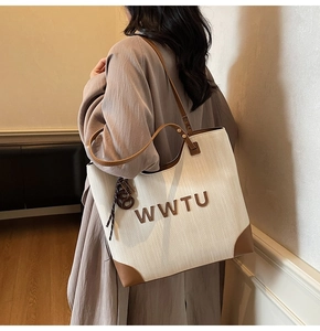 Detail of large tote bag showing woven texture, leather handles and 3D letter logo