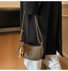 Brown suede crescent bag with stitching detail and beaded tassel charm on a model