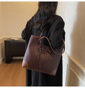 Model view of large brown woven tote bag with leather corners and embossed logo