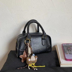 Detail of black Boston bag with pebbled leather texture, bear charm, and gold zipper hardware