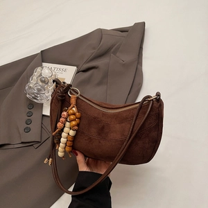 Detail of a brown suede croissant crescent bag with retro beaded tassel and metal zipper