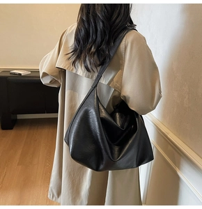 Lifestyle view of a large black faux leather hobo bag worn by a model in a minimalist room