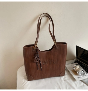 Detail of brown tote bag with vertical stripes, MWTU embossed logo and stylish woven charm