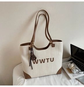 Close-up of woven beige tote bag with brown leather trim and WWTU letter logo