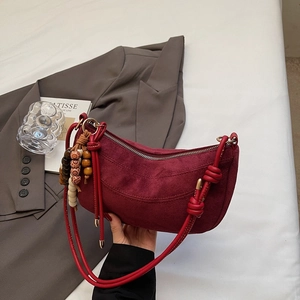 Detail of burgundy suede croissant bag with retro beads and a decorative knotted strap