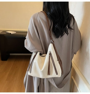 Detail of cream hobo bag featuring dark brown tassels and vertical zipper pockets
