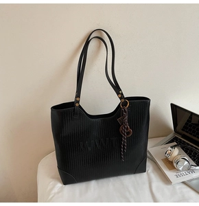 Detail of black woven texture tote bag with embossed letters and stylish tassel accent