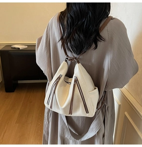 Detail view of a cream shoulder bag featuring vertical metal zippers and thin brown straps
