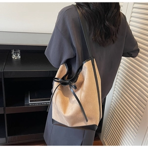 Side view of chic beige bucket bag with black leather straps and bow detail