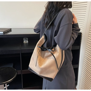Detail of apricot suede tote bag with black leather trim and decorative bow tie strap