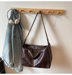 Detail of dark brown leather tote bag hanging with denim jacket and headphones