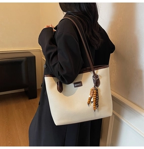 Close-up of canvas tote bag with brown leather trim and retro wooden bead pendant detail