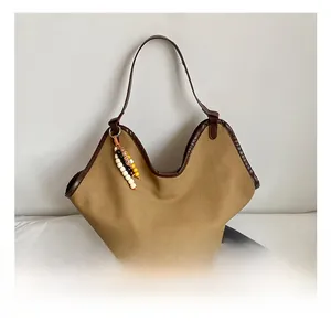 Detail view of khaki canvas tote with brown leather trim and decorative wooden bead charm
