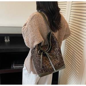 Detailed view of leopard print tote bag with green bow detail worn by a model