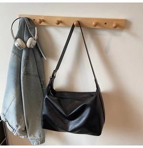 Detail of a black leather tote bag with wide straps and gold buckles on a wooden hanger