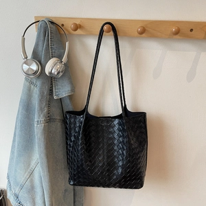 Close-up of matte black woven leather tote bag texture and long shoulder strap detail